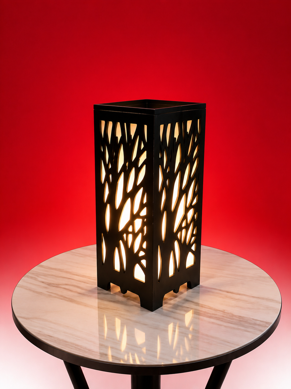 A black metal lantern with a tree branch cutout pattern, glowing with warm light, displayed on a round marble-top table against a solid red background.